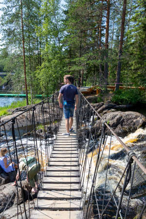 Ruskeala, Russia - July 10, 2021: People cross the suspension bridge over Ruskeala waterfall on the Tohmajoki river in the Republic of Karelia in Russiaのeditorial素材