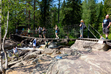Ruskeala, Russia - July 10, 2021: People cross the suspension bridge over Ruskeala waterfall on the Tohmajoki river in the Republic of Karelia in Russiaのeditorial素材