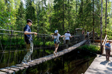 Ruskeala, Russia - July 10, 2021: People cross the suspension bridge over Ruskeala waterfall on the Tohmajoki river in the Republic of Karelia in Russiaのeditorial素材