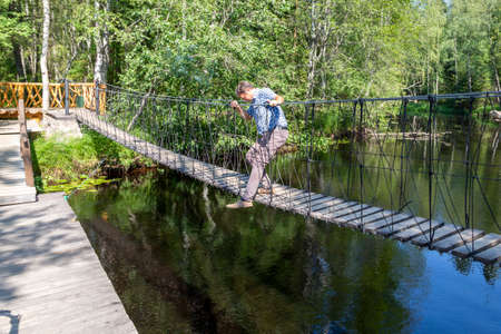 Ruskeala, Russia - July 10, 2021: A man tries to sit on a wooden suspension bridge at Ruskeala waterfalls on the Tohmajoki river in the Republic of Karelia in Russiaのeditorial素材