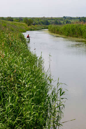 Summer water landscape with a fisherman on the river bank