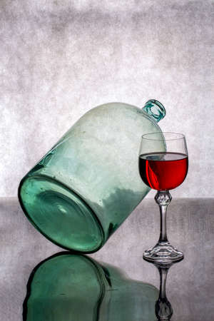 Still life with a tilted glass jar and a glass of red wineの写真素材