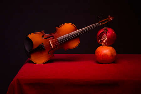 Still life with violin and ripe grenades on a red table