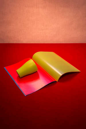 Still life with a green glass and notebook with colored sheets on a red table