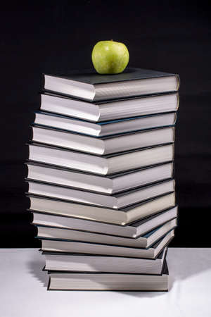 A green apple on a stack of books on a black background