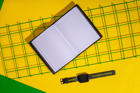 An open notepad and a smart watch on a metal grid on a yellow background