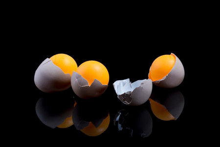 Still life with eggshell and orange balls on a black background