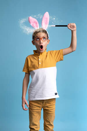 Studio photography on a blue background of a young child boy dressed in yellow magically making...