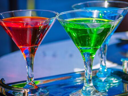 Red, blue, yellow, green and black drinks of different densities and poured into glass containersの写真素材