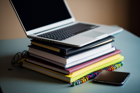 Stack of books with laptop on top of it next to pile of notebooks. Generative AI.の素材