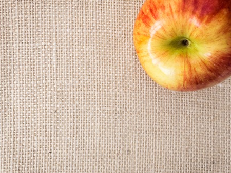 Fresh ripe apple on canvas background, close-up of red-yellow apple lying on jute canvas in corner...