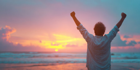 A powerful image of a man raising his arms in triumph against a vibrant sunset over the ocean, symbolizing success, freedom, and the joy of achievement in a beautiful, natural settingの素材