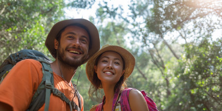 A happy couple with backpacks smiles brightly at the camera while enjoying a refreshing hike through a lush, green forest, epitomizing the joy of outdoor adventure and togethernessの素材