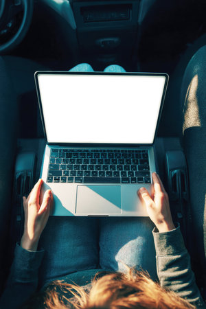 Top-down view of a person in a car's passenger seat using a laptop with a blank screen to work. Concept for remote work, mobile office, business travel, digital nomad, and on-the-go productivity and connectivity.の素材
