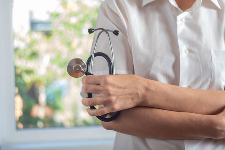 the doctor stands at the window and holds a stethoscope in his handの写真素材