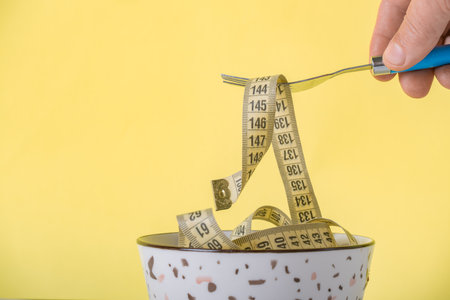 Measuring tape in a bowl with spoon on yellow background. Diet concept.