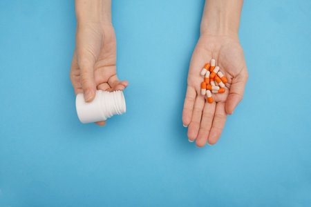 Top view of female hands with pills and bottle on blue background.の写真素材