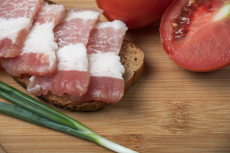 Slices of bread with bacon and tomatoes on a cutting boardの写真素材