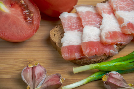 Slice of bread with bacon, tomato and garlic on wooden tableの写真素材