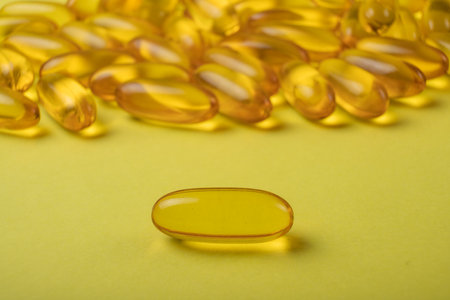 Cod liver oil omega 3 gel capsules on yellow background. Health care and medical concept.の写真素材