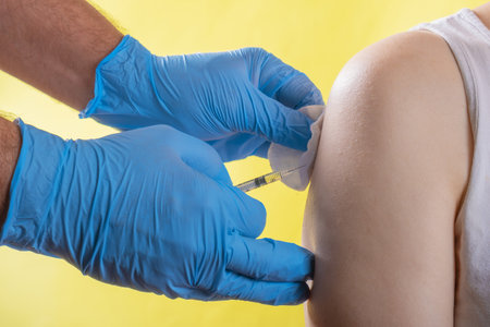 Doctor in blue gloves makes a vaccine to a woman on a yellow backgroundの写真素材