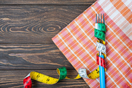 Fork and measuring tape on a wooden background. Diet concept.の写真素材