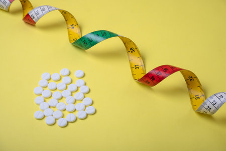 The concept of a healthy lifestyle with pills and measuring tape on a yellow backgroundの写真素材
