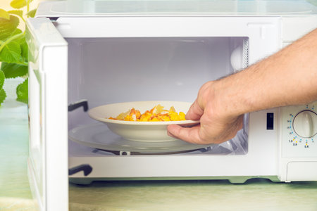 Man's hand holding a plate with baked potatoes in the microwave.の写真素材