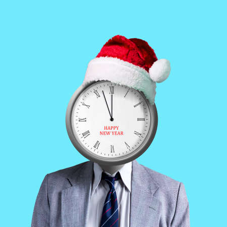 Businessman with a clock instead of a head. Hands of the clock at 12. Isolated on light blue background. Santa's hat. New Year. Holidays.の写真素材