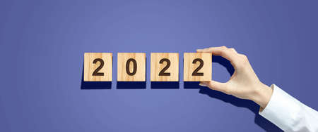 Hand holds a cube with 2022 numbers on wooden blocks. Hard shadow New Year's banner. Festive...