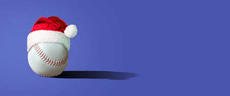Baseball ball in Santa Claus hat, on a blue background. Copy space. Place for your text. New Year's banner. Festive background.の写真素材