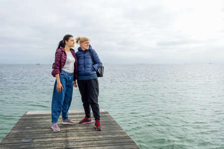 Two beautiful women look at the sea from a wooden pier. Freedom. Travel. Lifestyle.の写真素材