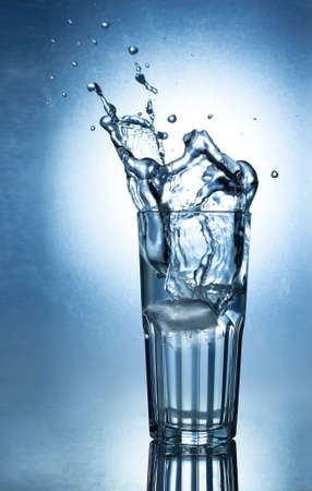 Splashing water of ice in a cool glass of water on a blue backgroundの写真素材