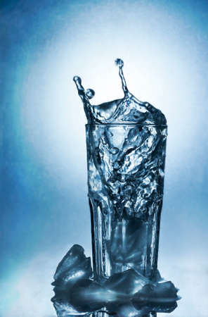 Splashing water of ice in a cool glass of water on a blue backgroundの写真素材
