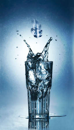 Splashing water of ice in a cool glass of water on a blue backgroundの写真素材
