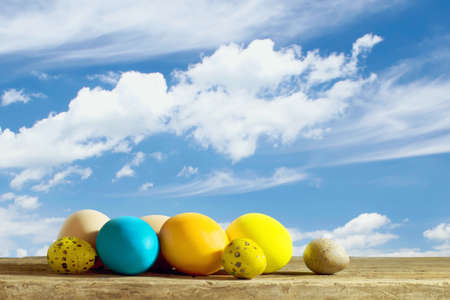 Easter background with multicolored Easter eggs on a wooden table against the blue sky. Copy space. Festive background.の写真素材