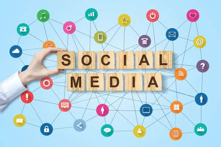 Social media concept with female hand and social icons on wooden blocks. Blue background