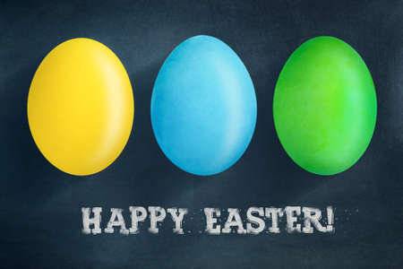 Multi-colored Easter eggs on a dark blue background. The inscription in chalk, Happy Easter. Easter background. Festive background.の写真素材