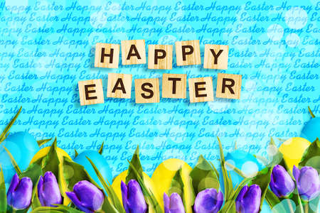 Happy Easter, word written on wooden blocks on blue background with multicolored easter eggs and tulips. Copy space. Place for text. Easter. Background.の写真素材