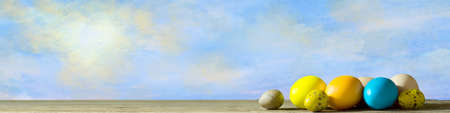 Easter background with multicolored Easter eggs on a wooden table against the blue sky. Copy space. Festive background.の写真素材