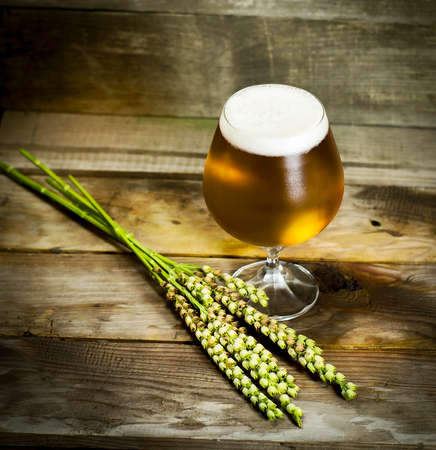 Glass of cold beer with wheat spikelets on wooden background.の写真素材