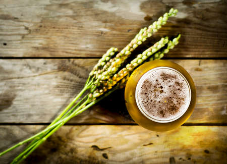 Glass of cold beer with wheat spikelets on wooden background. Top viewの写真素材