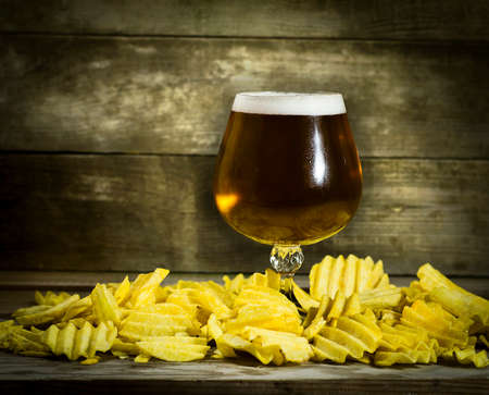 Glass of cold beer with chips on a wooden background.の写真素材