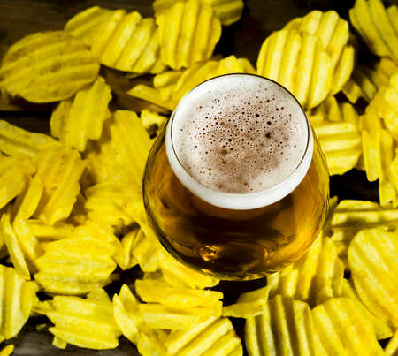 Glass of cold beer with chips on a wooden background.の写真素材