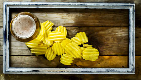 Glass of cold beer and chips in the old frame. On a wooden backgroundの写真素材