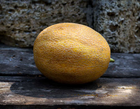 Ripe melon on a wooden table and a stone background
