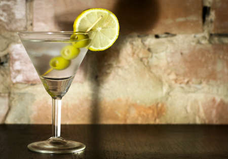 Martini with olives, lemon and ice on a background of an old brick wallの写真素材