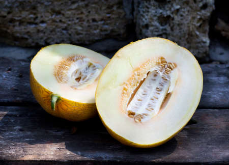 Ripe cut melon on a wooden table and a stone backgroundの写真素材