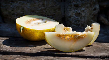 Ripe cut melon on a wooden table and a stone backgroundの写真素材