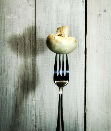 Fresh mushroom on a fork. On white wooden backgroundの写真素材